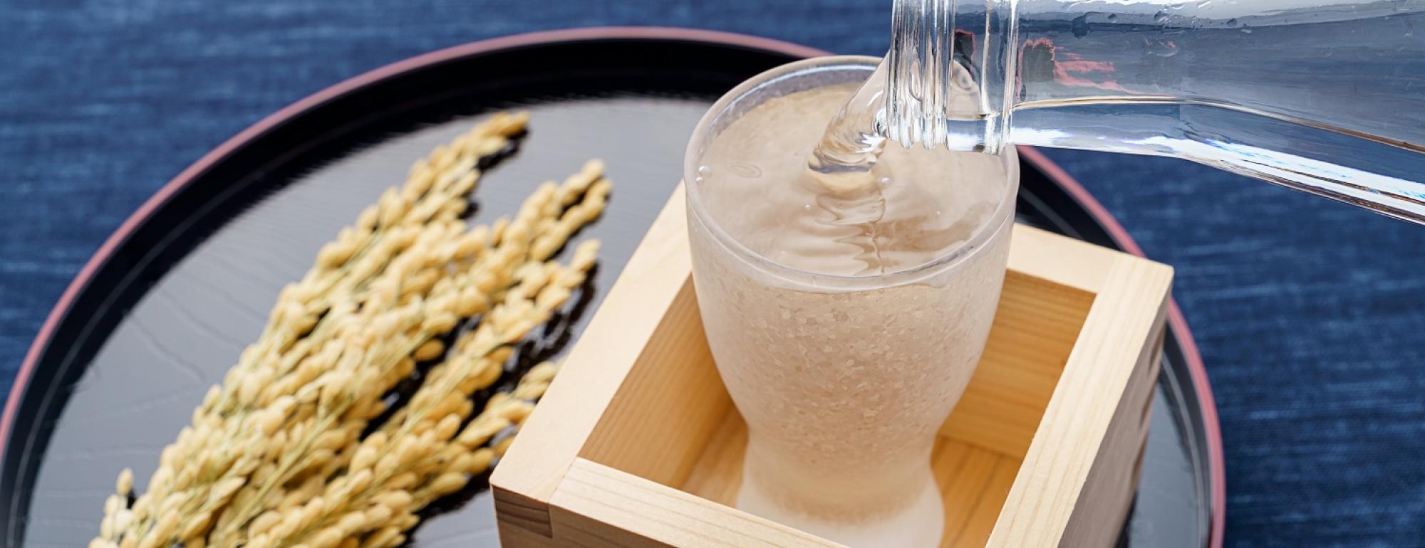 sake pouring into a glass inside a wooden cup with rice on the side