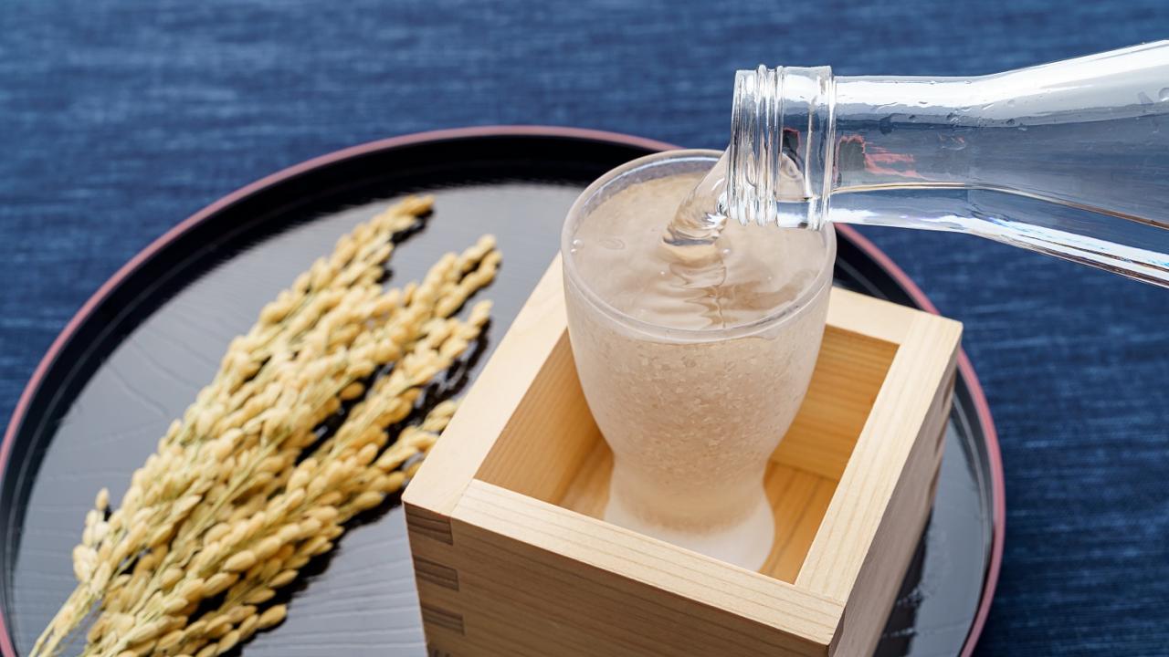 sake pouring into a glass inside a wooden cup with rice on the side