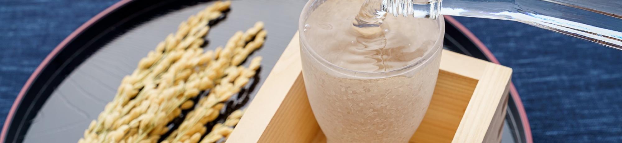 sake pouring into a glass inside a wooden cup with rice on the side